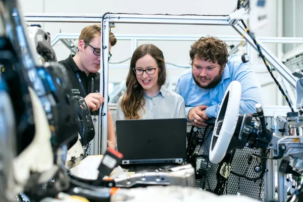 Three people - 2 man and 1 woman looking at laptop in manufacturing environment.